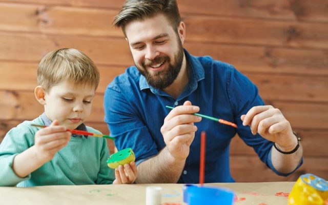 Smiling bearded young man in blue denim shirt paints fruit with a child