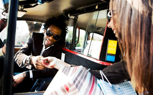 A smiling taxi driver takes payment from a happy passenger